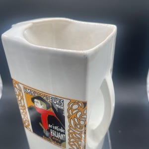 May include: White ceramic mug with a handle, featuring a vintage poster design with the text "Ambassadeurs Aristide Bruant dans son cabaret".