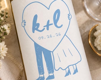 May include: A glass wine bottle featuring a white label with a light blue illustration of two figures holding a large heart. The heart contains the blue text k+l and the date 09.26.26. The figures are depicted from the waist down in blue.
