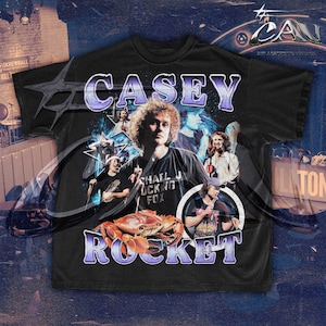 Może przedstawiać: Czarny T-shirt z nadrukiem graficznym zespołu o nazwie "Casey Rocket". Grafika przedstawia kolaż członków zespołu, kraba i tekst "Shall I Ducking Fox".