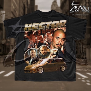 Può includere: T-shirt nero con un design dorato "HECTOR" e un ritratto di un uomo, insieme a una grafica di un'auto dorata. Il design incorpora più immagini dell'uomo e di altri. La maglietta ha un girocollo.