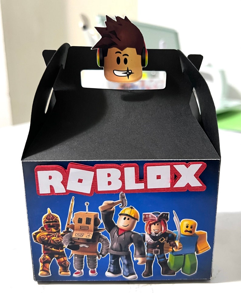 May include: A black favor box with a blue background and the word "ROBLOX" in red and white letters. The box features a variety of Roblox characters, including a knight, a robot, a construction worker, a pirate, and a yellow character with a surprised expression.