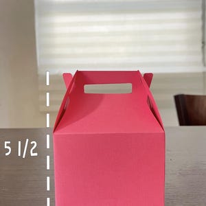 May include: A small, bright pink gift box with a handle. The box measures 5 1/2 inches tall and 4 1/4 inches wide.