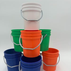 May include: A stack of six plastic buckets in various colors, including white, orange, green, and blue. The buckets are all the same size and have a silver handle.