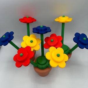 May include: A colorful flower pot with six flowers in red, yellow, and blue. The flowers have green centers and are attached to green stems.