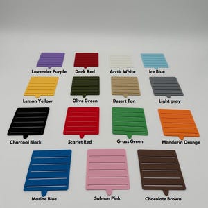 May include: A collection of 15 color swatches, each with a different color name printed below. The swatches are arranged in three rows of five. The colors include lavender purple, dark red, arctic white, ice blue, lemon yellow, olive green, desert tan, light gray, charcoal black, scarlet red, grass green, mandarin orange, marine blue, salmon pink, and chocolate brown.