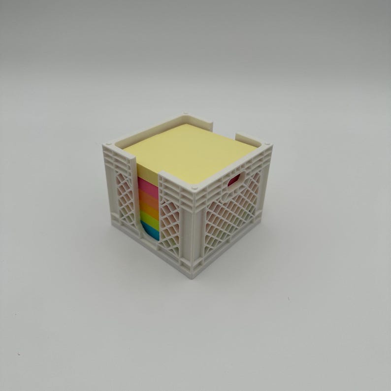May include: A white plastic crate with a stack of colorful sticky notes inside. The top note is yellow, and the rest are rainbow-colored.