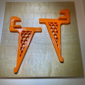 May include: Two orange plastic shelf brackets with a honeycomb design. The brackets are angled and have a lip on the top.