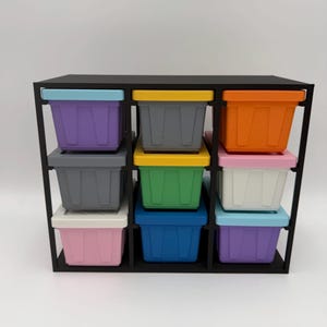 May include: A black storage organizer unit featuring nine individual square bins arranged in a three-by-three grid. Each bin has a solid-colored base and a contrasting lid, showcasing a variety of colors including purple, gray, orange, yellow, green, white, pink, and blue.
