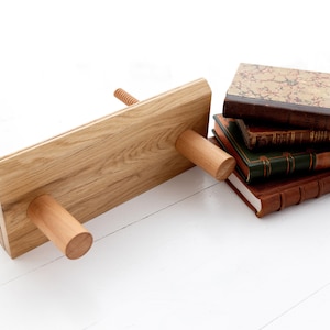 May include: A wooden bookend with three wooden pegs and a natural wood finish. The bookend is holding up a stack of four antique books with leather covers.