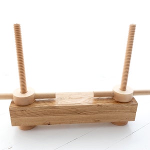 May include: A wooden clamp with two threaded screws and a wooden handle on each side. The clamp is made of natural wood and has a rustic look.