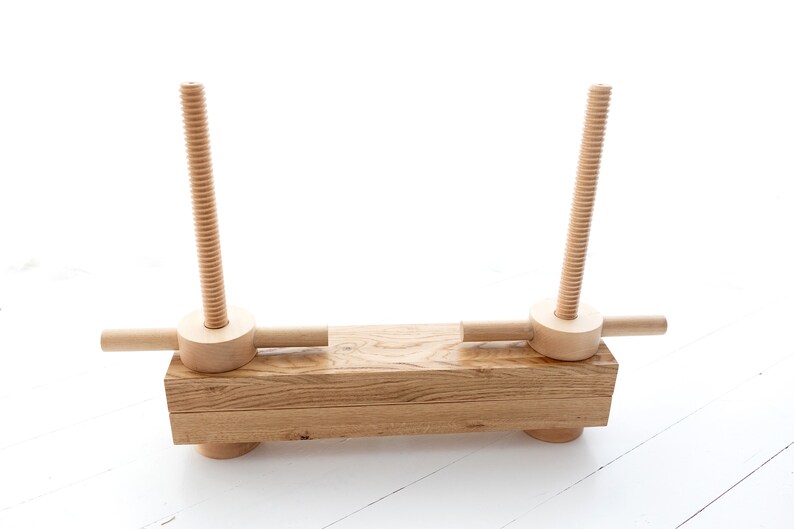 May include: A wooden clamp with two threaded screws and a wooden handle on each side. The clamp is made of natural wood and has a rustic look.