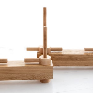 May include: Two wooden clamps with threaded screws and handles. The clamps are made of light brown wood and are in a horizontal position.