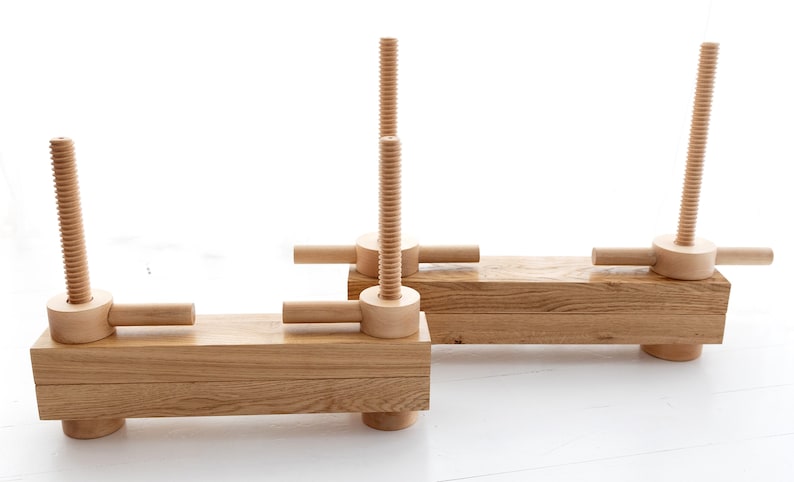 May include: Two wooden clamps with threaded screws and handles. The clamps are made of light brown wood and are in a horizontal position.