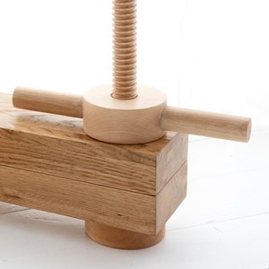May include: Close-up of a wooden clamp with a threaded screw and a wooden handle. The clamp is made of light-colored wood and has a natural finish.