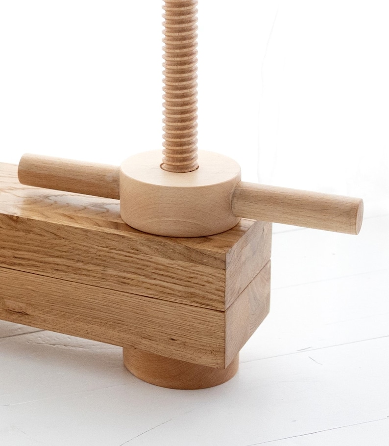 May include: Close-up of a wooden clamp with a threaded screw and a wooden handle. The clamp is made of light-colored wood and has a natural finish.