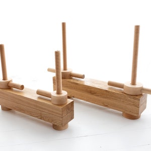 May include: Two wooden clamps with threaded screws and handles. The clamps are made of natural wood and have a rustic look.
