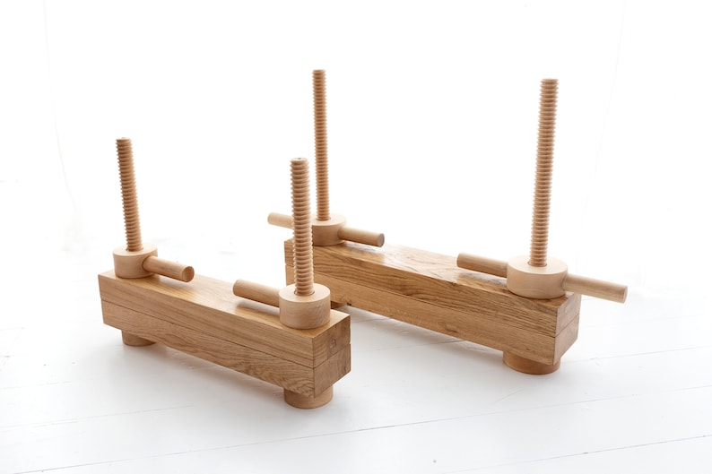 May include: Two wooden clamps with threaded screws and handles. The clamps are made of natural wood and have a rustic look.