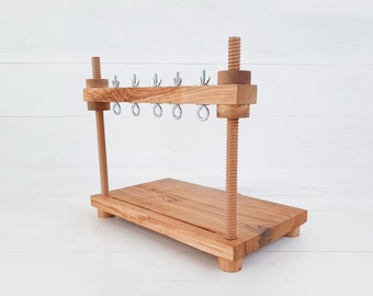 May include: Wooden frame with a threaded rod and multiple hooks. The frame is made of light brown wood and has a rectangular base.
