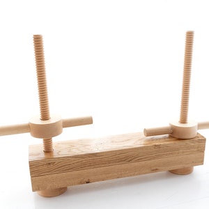 May include: A wooden clamp with two adjustable screws and a long wooden base. The clamp is made of natural wood and has a rustic look.