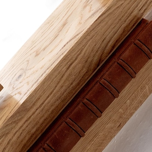 May include: Close-up of a wooden shelf with a brown leather-bound book resting on top. The shelf has a natural wood grain and is made of solid wood.