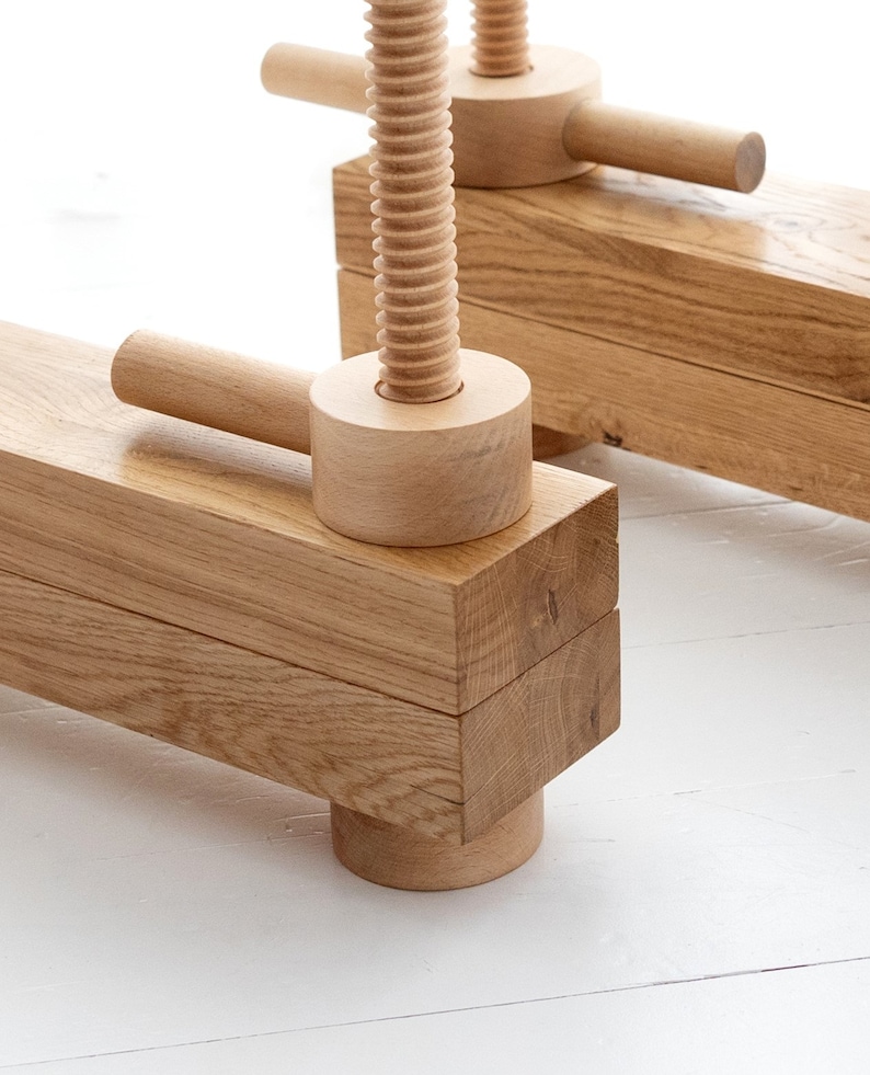 May include: A wooden clamp with a threaded screw and two handles. The clamp is made of natural wood and has a rustic look.