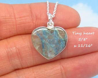 May include: A silver necklace with a heart-shaped pendant. The pendant is 5/8" x 11/16" and features a blue and white stone. The necklace is displayed on a hand against a blue background. The text "Tiny heart" is visible.