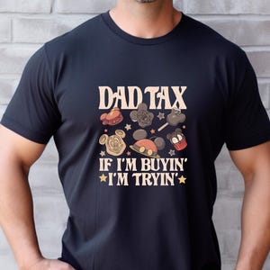 May include: Black t-shirt with the text "DAD TAX" above a collection of cartoon images and the phrase "IF I'M BUYIN' I'M TRYIN'". The design features Mickey Mouse and other theme park-related graphics in shades of brown, red, and yellow.