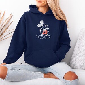 May include: Navy blue hoodie featuring a white sketch of Mickey Mouse. The cartoon character has a red and white outfit. The hoodie has a front pocket and a drawstring hood. The sweatshirt is made of a soft material.