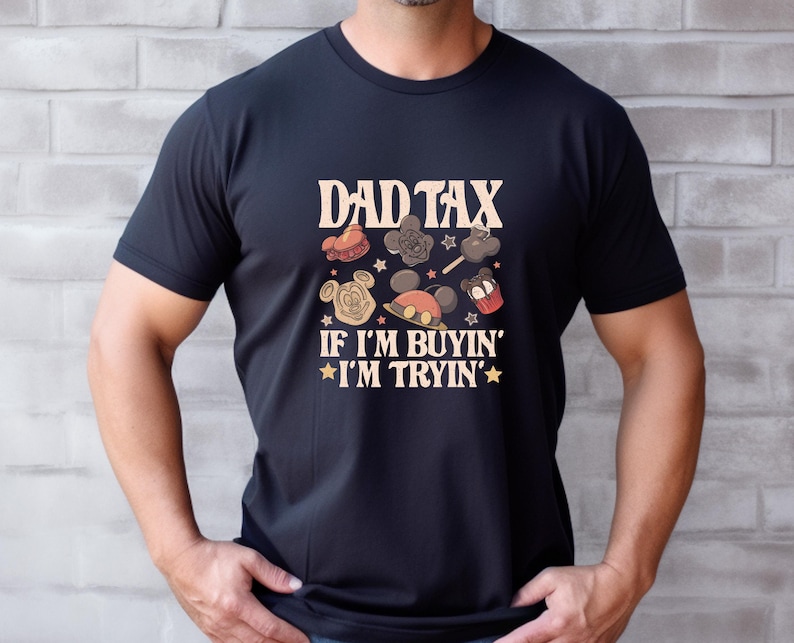 May include: Black t-shirt with the text "DAD TAX" above a collection of cartoon images and the phrase "IF I'M BUYIN' I'M TRYIN'". The design features Mickey Mouse and other theme park-related graphics in shades of brown, red, and yellow.