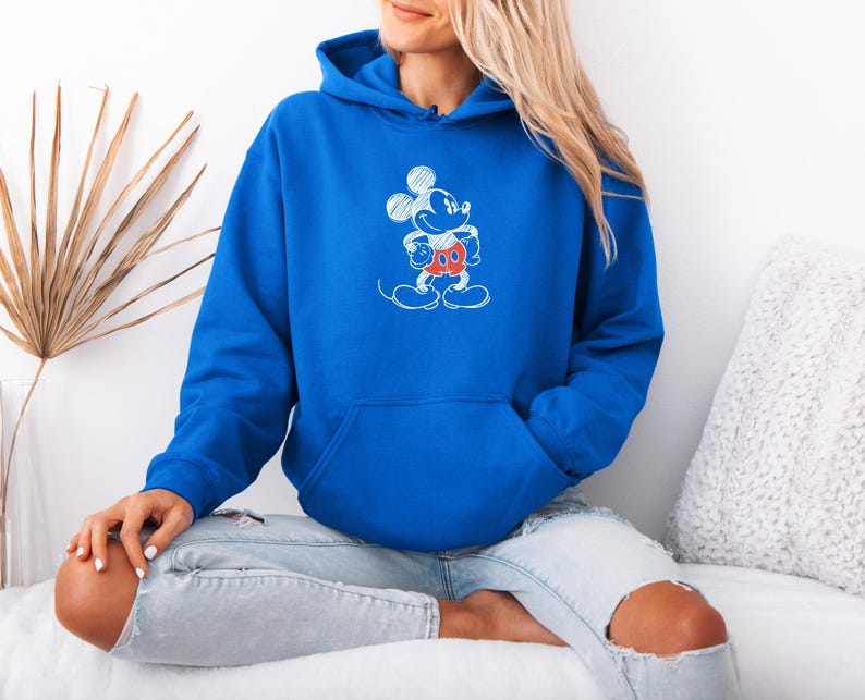 May include: Royal blue hoodie with a white and red Mickey Mouse sketch design. The hooded sweatshirt has a front pocket and a drawstring hood. The graphic features Mickey Mouse in a standing pose. The hoodie is made of a soft material.