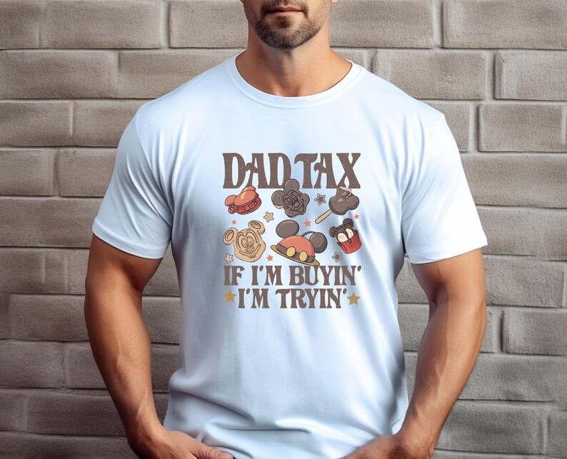 May include: Light blue t-shirt with the text "DAD TAX" above cartoon images of treats and the phrase "IF I'M BUYIN' I'M TRYIN'". The shirt features a crew neck and short sleeves.