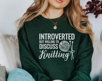 May include: A green sweatshirt with the text "Introverted but willing to discuss knitting" and a white illustration of a ball of yarn and knitting needles.