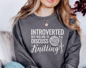 May include: A gray sweatshirt with the text "Introverted but willing to discuss knitting" and a graphic of a ball of yarn and knitting needles.