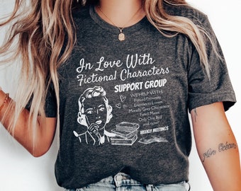 May include: Dark gray t-shirt with the text "In Love With Fictional Characters SUPPORT GROUP". The graphic includes a vintage illustration of a woman, books, and additional text about the group's focus. A literary-themed apparel item.