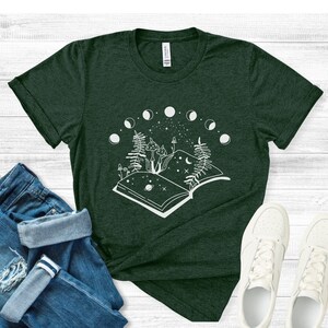May include: A dark green t-shirt with a white graphic of an open book with mushrooms and ferns growing out of it. The book is surrounded by a circle of moons.