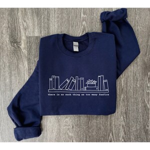 May include: Navy blue sweatshirt with a white graphic of a bookshelf and the text "there is no such thing as too many fanfics." The long-sleeved top is made of a soft material.