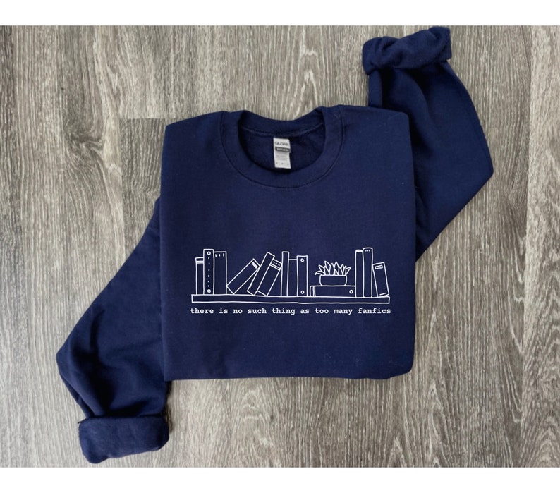 May include: Navy blue sweatshirt with a white graphic of a bookshelf and the text "there is no such thing as too many fanfics." The long-sleeved top is made of a soft material.