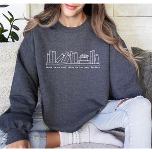 May include: Dark gray sweatshirt with a white graphic of a bookshelf and the text "there is no such thing as too many fanfics". The sweatshirt is made of a soft material.