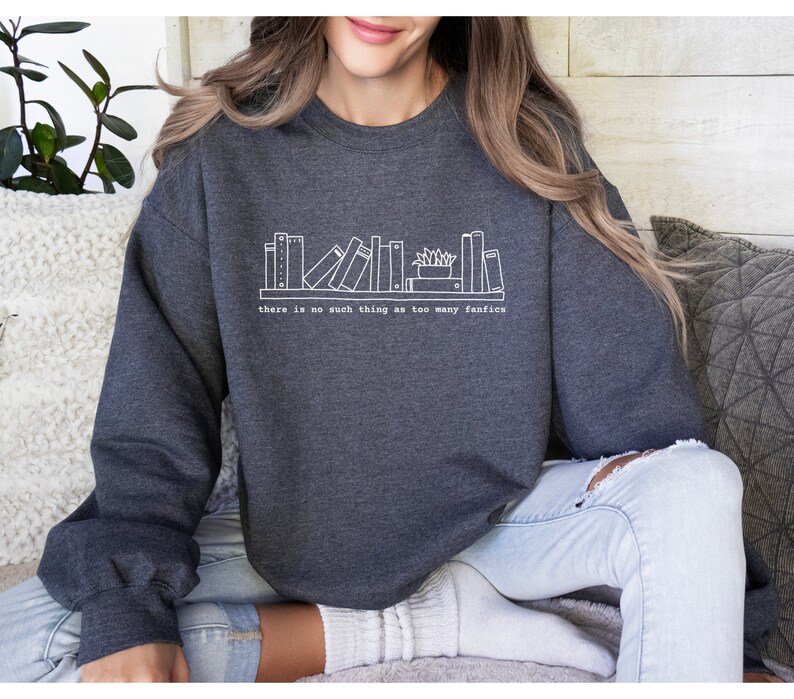 May include: Dark gray sweatshirt with a white graphic of a bookshelf and the text "there is no such thing as too many fanfics". The sweatshirt is made of a soft material.