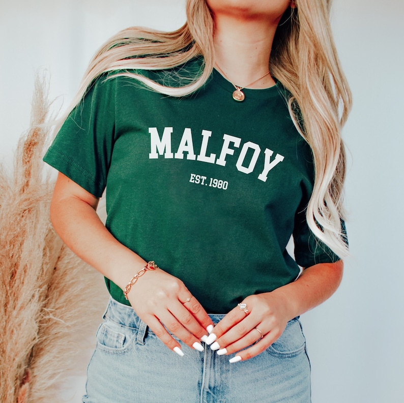 May include: A green t-shirt with white text that reads "MALFOY EST. 1980".
