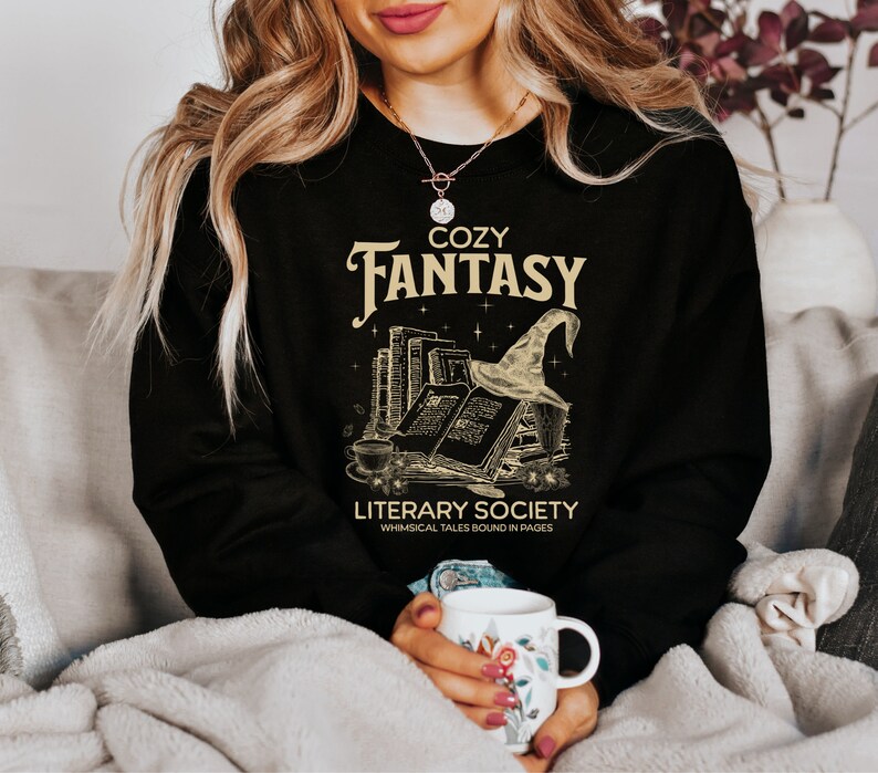 May include: Black sweatshirt with a gold graphic of a stack of books, a witch's hat, and the text "Cozy Fantasy Literary Society Whimsical Tales Bound in Pages".