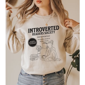 May include: A beige sweatshirt with a black graphic design that says "Introverted Readers Society" and includes a drawing of a person reading a book. The text also says "Meets monthly but usually cancels at the last minute".
