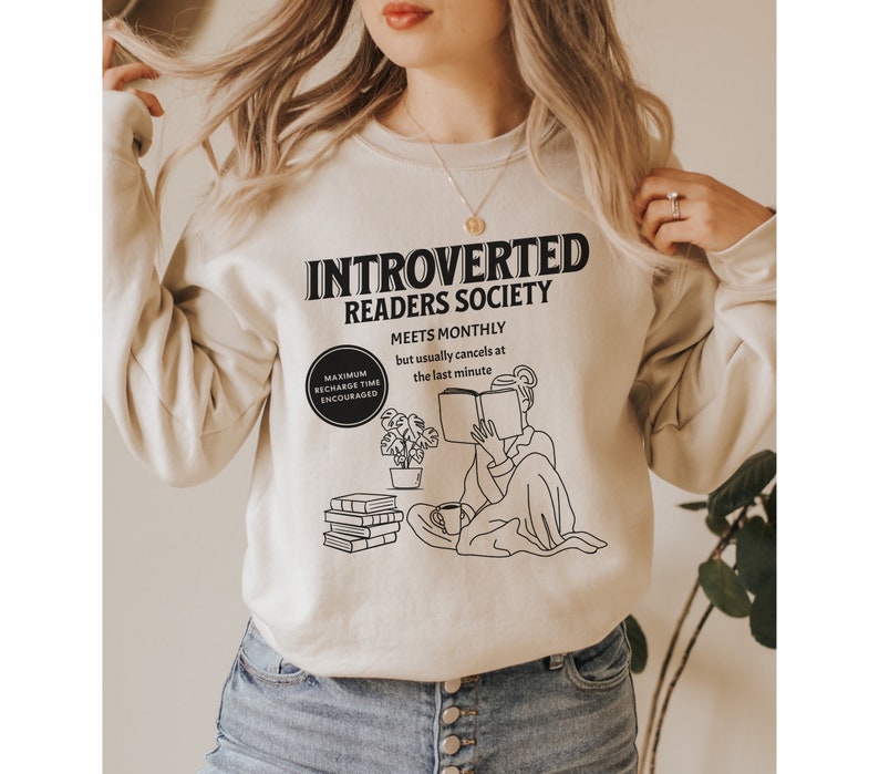 May include: A beige sweatshirt with a black graphic design that says "Introverted Readers Society" and includes a drawing of a person reading a book. The text also says "Meets monthly but usually cancels at the last minute".