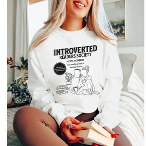 May include: White sweatshirt with a black graphic design that reads "Introverted Readers Society" and "Meets Monthly but usually cancels at the last minute". The graphic also includes a line drawing of a person reading a book.