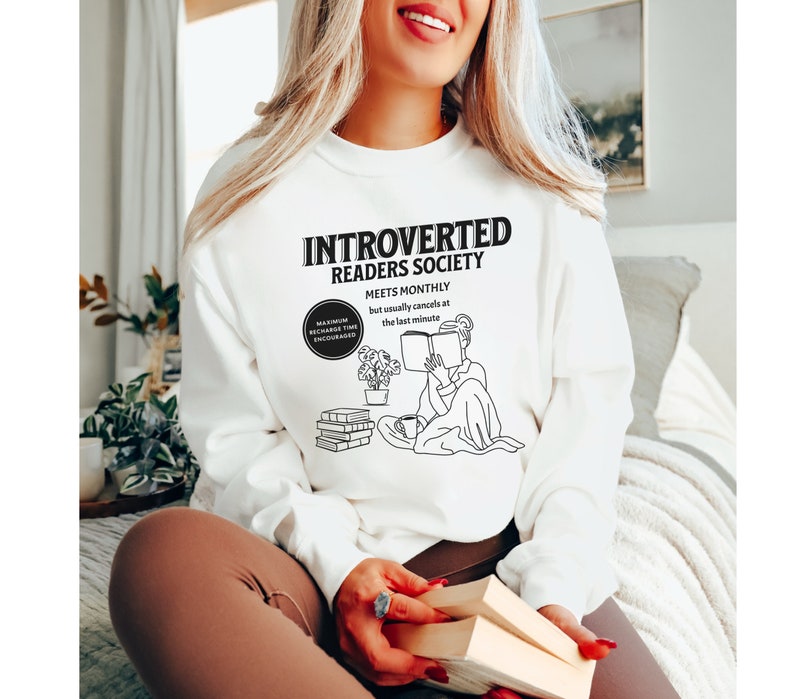 May include: White sweatshirt with a black graphic design that reads "Introverted Readers Society" and "Meets Monthly but usually cancels at the last minute". The graphic also includes a line drawing of a person reading a book.