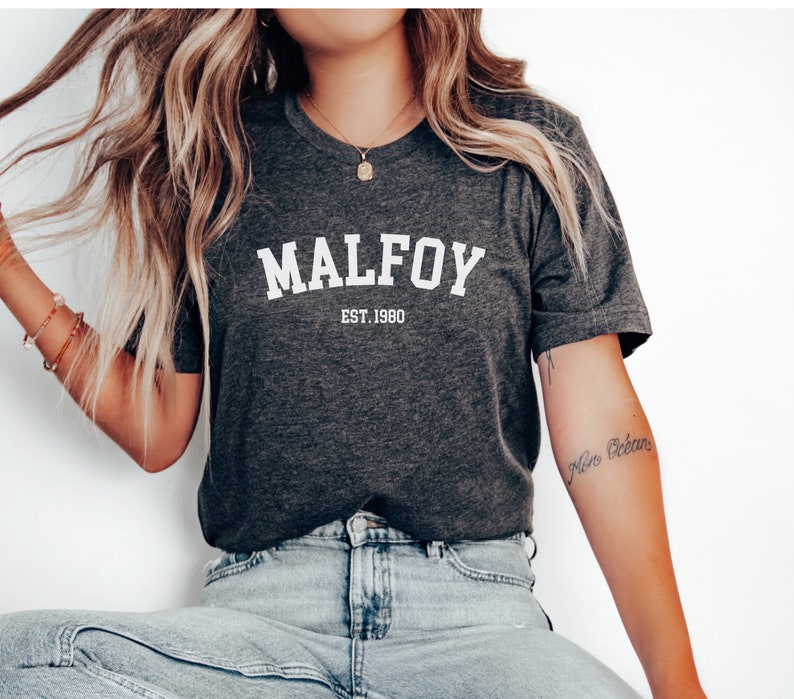 May include: A dark grey t-shirt with white text that reads "MALFOY EST. 1980".