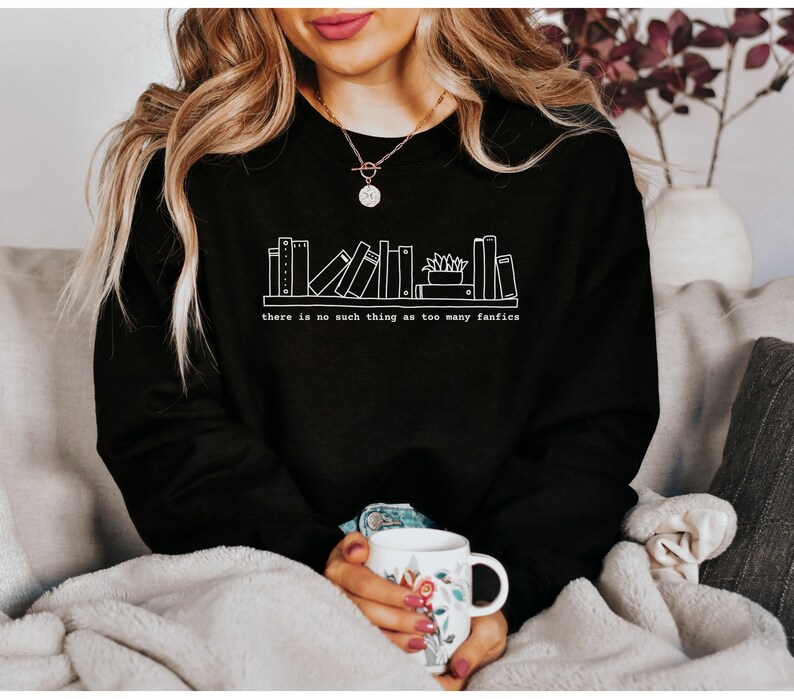 May include: Black sweatshirt with a white graphic of a bookshelf and the text "there is no such thing as too many fanfics". The sweatshirt is made of a soft material.