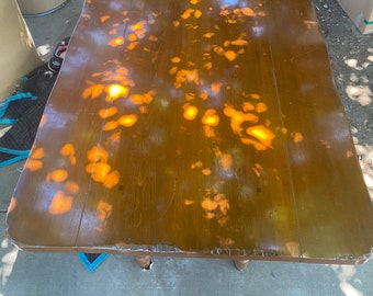 Könnte beinhalten: Eine Tischplatte aus Holz mit einer natürlichen Holzmaserung. Die Tischplatte ist hellbraun und von geflecktem Sonnenlicht bedeckt. Die Tischplatte ist glatt und hat einen leichten Glanz.