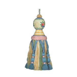 May include: A decorative tassel featuring a spherical top painted with floral and geometric patterns in red, green, and yellow. Below the sphere is a yellow checkered neck, a pink textured band, and a skirt of blue, green, and yellow threads.