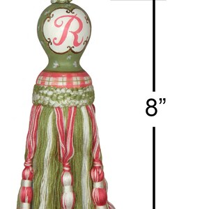 Puede incluir: Borla verde y rosa con una parte superior de madera pintada con la letra "R" en rosa. La borla mide 8 pulgadas de largo y tiene un lazo de 6 pulgadas.